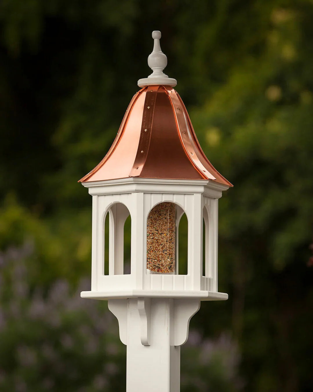 Decorative bird feeder with copper roof against a blurred green background